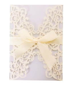Macro shot of glitter paper wedding invitation with laser-cut floral patterns and beige bow