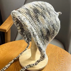 Detail of chunky knit ear-flap hat with mixed grey and white yarn texture on stand