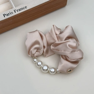 Detail van een roze satijnen scrunchie met elegante witte parels op beige basis