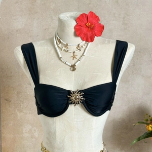 Détail du haut de bikini noir avec boucle soleil dorée centrale et tissu plissé chic