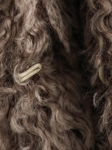 Macro view of warm camel faux fur texture with curly plush pile and woven rope loop closure