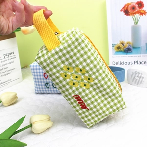 Close-up of green checkered makeup bag with flower embroidery and yellow ribbon handle