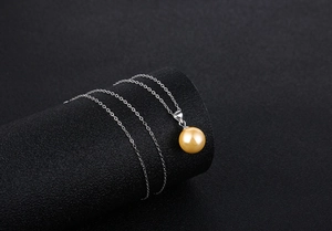 Detailed view of large golden pearl pendant on fine silver chain over black pedestal