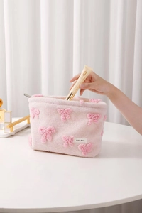 Detail of pink plush makeup bag with bow decoration being filled with skincare products