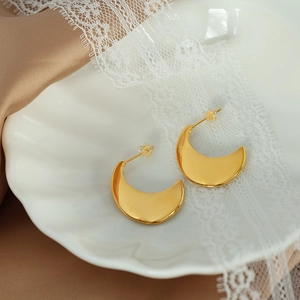 French minimalist golden crescent moon stud earrings on white shell plate and brown silk