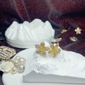 Sparkling gold flower stud earrings with crystals on a textured white stone display base