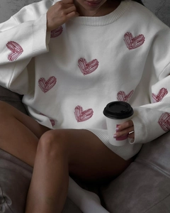 Detail of white knit sweater with red heart patterns and round neck in cozy lifestyle scene
