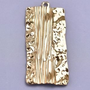 Macro shot of a 18k gold plated rectangular pendant with hammered metal texture