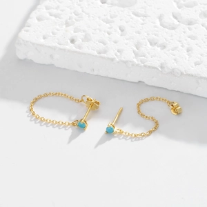 Detail of gold chain earrings with sky blue stones on a white natural stone base