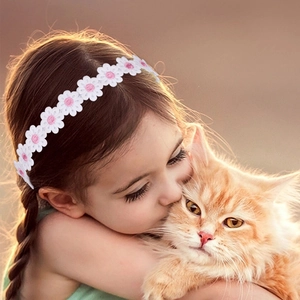 Close-up of baby wearing a soft white daisy headband while hugging a cute orange cat