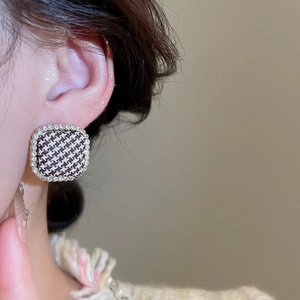 Close-up detail of silver stud earrings with houndstooth fabric and sparkling crystals