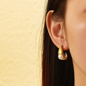 Close-up of elegant gold curved metal stud earrings featuring a lustrous white pearl