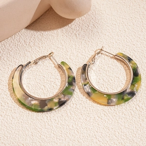 Detailed shot of C-shaped acetate hoop earrings with green marbled texture on a textured stone