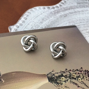 Macro view of knotted S925 silver stud earrings with a hollow and polished metal finish