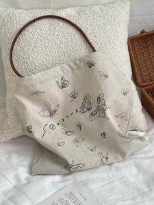 Detail of butterfly print canvas tote featuring brown leather circular handles and soft texture