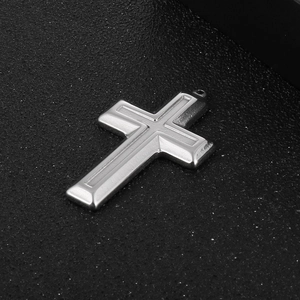 Close-up of polished silver stainless steel cross pendant on black textured surface