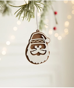 Close-up of a wooden Santa Claus ornament hanging on a pine tree branch with warm bokeh