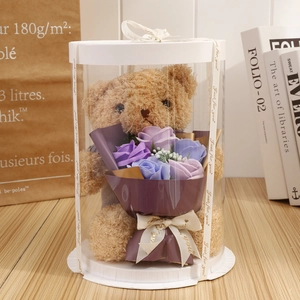 Close-up of a plush brown teddy bear with purple soap flowers in a clear round gift box