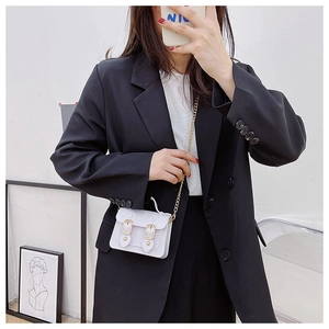 White mini crossbody Cambridge bag with gold chain strap shown on a black suit