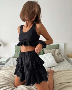 Detail of black lace-edged crop top and layered ruffle skirt set on a soft bed