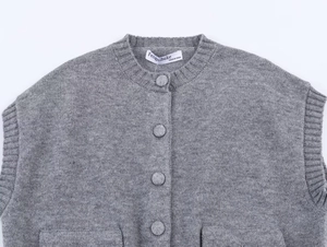 Détail du gilet en tricot gris avec col rond, boutons en tissu et texture douce