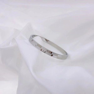 Minimalist silver titanium steel bangle with geometric checkerboard pattern on white silk