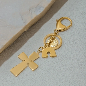 Close-up of golden stainless steel keychain with cross and rainbow charms on stone