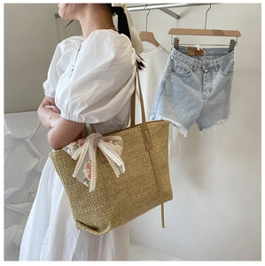 Detail showing lace bow with pink floral embroidery on a woven straw tote bag