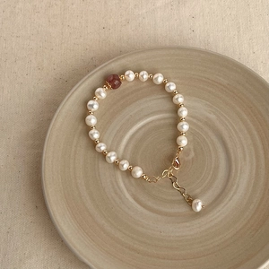 Close-up of baroque pearl bracelet with red gemstone and gold clasp on ceramic plate