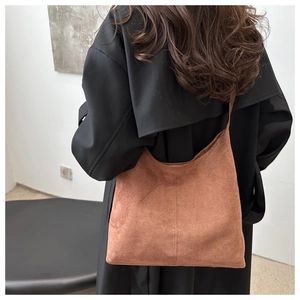 Close-up of brown suede tote bag on black coat showing premium texture and shoulder fit