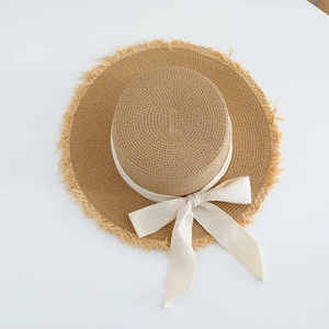 Close-up of flat top straw hat with bow ribbon and fringe brim detail on white background