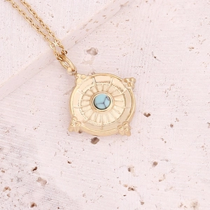 Macro view of a gold square pendant featuring a turquoise stone on a beige stone surface