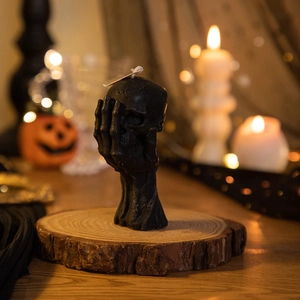 Detailed black skull candle with skeleton hand on wood stand for Halloween decor