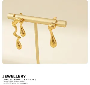 Dettaglio di orecchini asimmetrici in oro fluido su supporto con illuminazione morbida