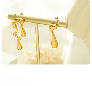 Detalle de pendientes asimétricos de oro fluido en un soporte con iluminación suave