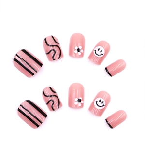 Pink press-on nails featuring black swirl lines, white daisies, and smiley face patterns