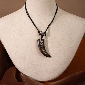 Close-up of Maori style fish hook pendant with brown carvings and black cord on mannequin