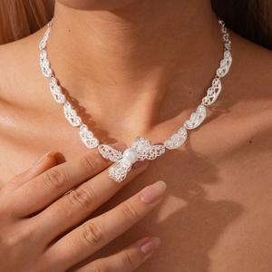 Close-up of silver bow pendant with white faux pearl on a delicate necklace for women