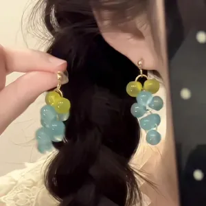 Close-up of yellow and blue grape-shaped beaded drop earrings on ear with gold hook