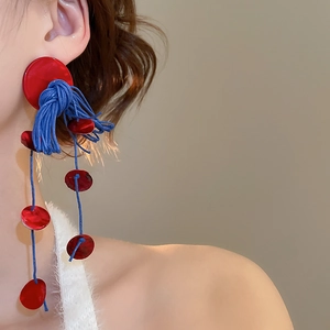 Detail of bohemian red shell and blue tassel drop earrings worn by a model