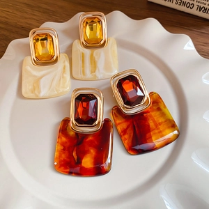 Detail of vintage square resin earrings with marble texture and rhinestone studs on a tray