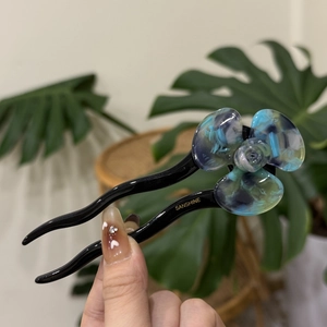 Close-up of a blue and purple resin flower hair pin with U-shaped black acetate tines