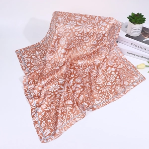 Detail view of orange floral silk scarf with cashew prints on white desk with plants