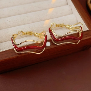 Detailed macro view of gold irregular wave hoop earrings with deep red enamel accents