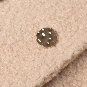 Macro view of light beige bouclé fabric texture with a hammered vintage metal button