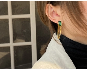Close-up of golden tassel earrings featuring rectangular green emerald gemstones on model
