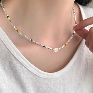 Close-up of a colorful beaded necklace featuring a white daisy pendant on a model's neck