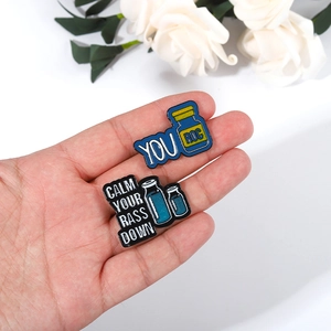 Broches en émail en forme de bouteilles bleues et noires avec des textes amusants tenues en main
