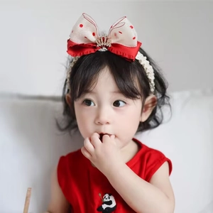 Close-up of a toddler wearing a red polka dot bow headband with a small crown detail