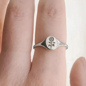 Silver signet ring with engraved sunflower design worn on finger in a minimalist style